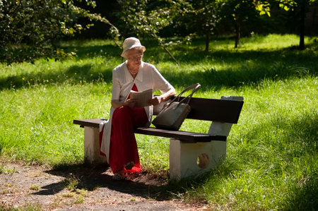 retired woman reading newspaper outdoors at parkの写真素材