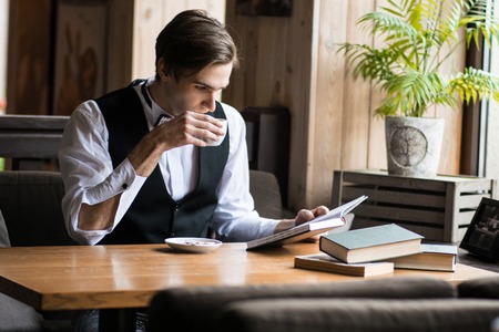 young, successful business man sitting in a cafe with a book and a cup of coffee in a white shirt and tieの写真素材