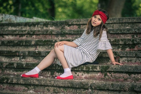 Little girl in casual clothes and shoes, sitting on stairsの写真素材