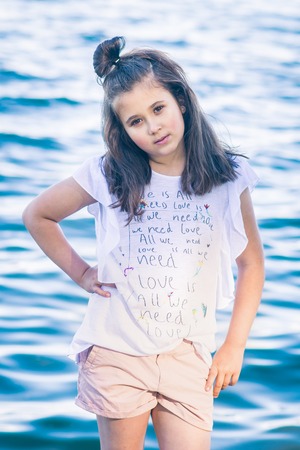 Portrait of little fashionable girl walking on berth near seaの写真素材