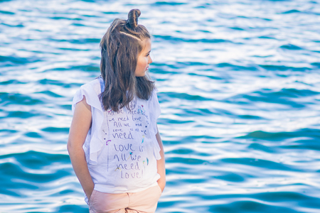 Portrait of little fashionable girl walking on berth near seaの写真素材