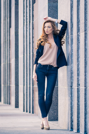 Outdoors fashion portrait of trendy pretty girl posing on the wall background.の写真素材