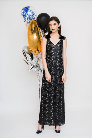 Joyful young woman in luxury dress on heels celebrating new year in studio. Having fun with balloonsの写真素材