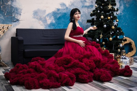 A young pregnant woman in a beautiful dress is sitting on the couch of a house that is being renovated.の写真素材