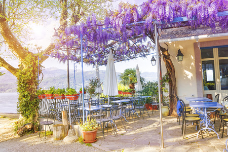 Terrace of outdoor small retro cafe decorated with flowers of wisteria on the Italian coast in a sunny spring evening. Lake Lago Maggiore in Stresa, Italyのeditorial素材