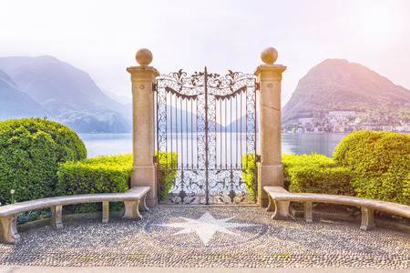Beautiful view of the lake surrounded by mountains through the gate in Ciani Park, in Lugano on spring morning, Ticino, Switzerlandの写真素材