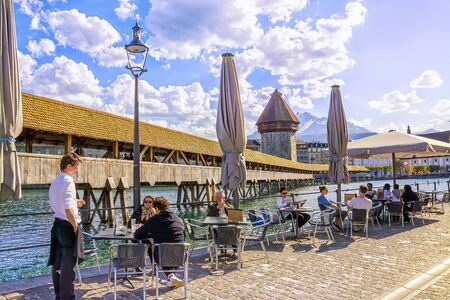 LUCERNE, SWITZERLAND - APRIL 10, 2017: Tourists rest in street restaurant with beautiful view on wooden Chapel Bridge Kapellbrucke and snow covered Pilatus Mountain in historic center of Lucerneのeditorial素材
