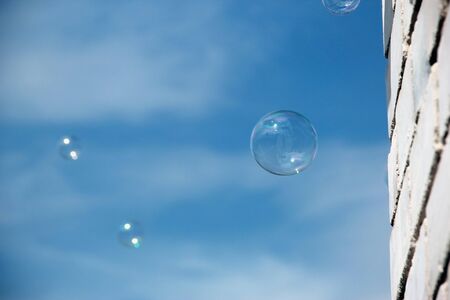 Transparent soap bubble on blue sky with clouds and white brick wall background. On a Sunny summer...