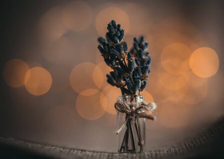 A small bouquet of lavender flowers on a brown background with Golden yellow bokeh light close-up. Bunch of lavender in a tiny bottle, vase, macro. Beautiful bright bokeh. Still life with flowers. Texture and background.の写真素材