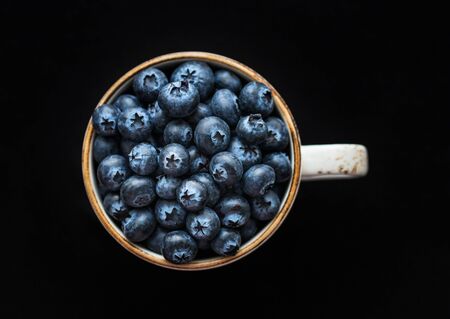Fresh blueberries in a cup on a black background. Top view, macro. Blue ripe berries closeup. Food background.の写真素材