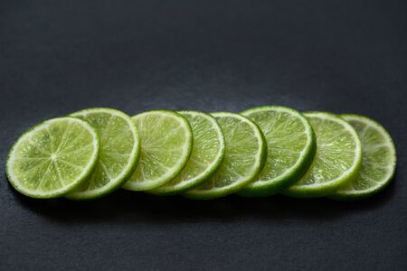 Sliced citrus fruit lime on a stone table. Food background. Juicy ripe slices of green lime on a black background. Side view close-up. Fresh ripe fruit.の写真素材