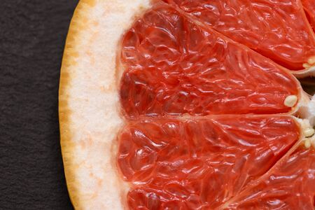 Sliced red grapefruit on black background closeup. Food background. Flat lay. Juicy ripe fresh...