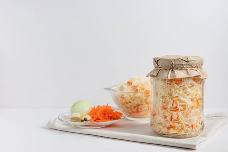 Homemade sauerkraut with carrots in a glass jar and bowl on a white wooden background. Fermented...