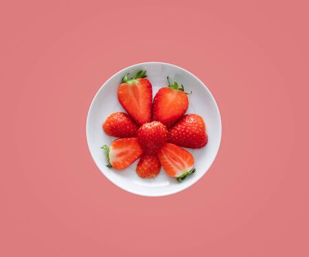 Food concept. Fresh juicy sliced strawberries in a white plate isolated on a pink background. Copy...