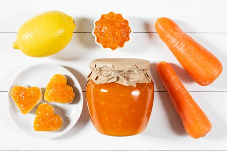 Homemade carrot jam with lemon in a glass jar on a white wooden background. Delicious toast in the shape of a heart with carrot jam. Top view, flat lay.の写真素材