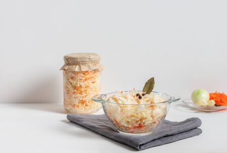 Homemade sauerkraut with carrots in a glass jar and bowl on a white wooden background. Fermented food. Copy space.の写真素材