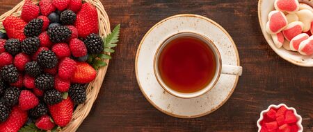 A cup of tea on the table with berries and sweets. Banner. Berry tea on a wooden background. Food tea concept. Top view, flat lay.の写真素材