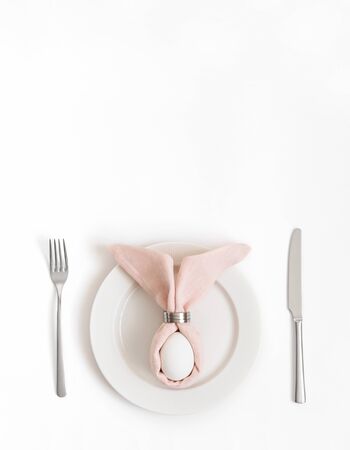 Easter table setting with egg in pink Easter bunny napkin on a white background. Vertical orientation. Copy space, top view, flat lay.の写真素材
