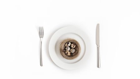 Easter table setting with quail eggs in a nest on a white background. Copy space, top view, flat lay.の写真素材