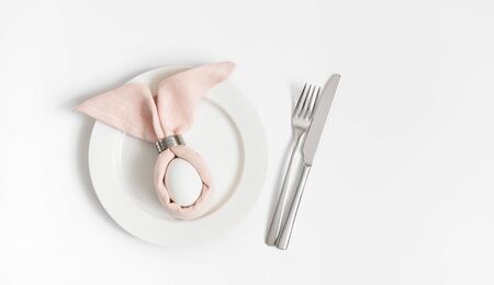 Easter table setting with egg in pink Easter bunny napkin on a white background. Copy space, top...