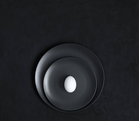 White egg on black plates on a dark background. Black minimal concept. Easter table setting....