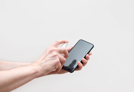 Mobile phone disinfection on a white background. Men's hands cleans the phone with a sanitizer spray. Prevention of coronavirus, covid-19. Protection concept.の写真素材