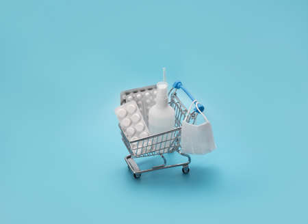 Toy shopping cart with medicines on a blue background. Concept of protection and prevention against...