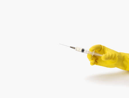 A hand in a yellow medical glove holds a syringe on a white background. Healthcare concept. Copy...