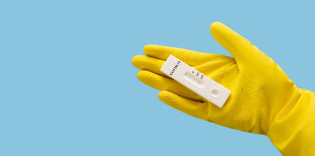 Unused covid-19 test in hand on a blue background. A hand in a yellow protective glove holds a test...