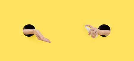 A woman uses an antibacterial spray on a yellow background. Personal hygiene concept. Protection and...
