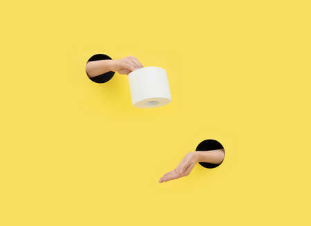 A female hand gives toilet paper on a yellow background. Hand in a paper hole. Help concept. Copy space.の写真素材