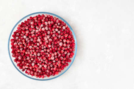 Frozen cranberry berries in a large transparent plate on a white background. Vitamins. Copy space,...