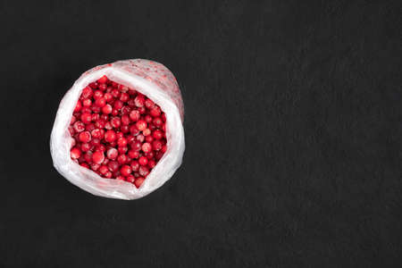 Frozen cranberry berries in a bag on a black background. Stocks concept. Frozen food. Space for...