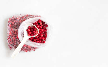 Frozen red berries in a bag with a spoon on a white background. Frozen cranberries. Concept of...