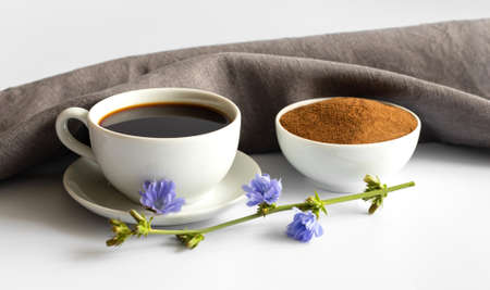 Cup with chicory drink, powder and blue flowers on white background. A useful coffee substitute. Side view.の写真素材