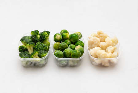 Frozen vegetables cabbage mix in containers on a white background. Brussels sprouts, broccoli,...