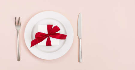 Festive table setting with a gift in a plate on a pink background. Banner. Space for text. Top view. Valentines Day, Mothers Day, Birthday or Christmas concept.の写真素材