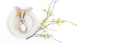A white egg with a gray Easter bunny napkin and yellow flowers on a white background. Easter table...