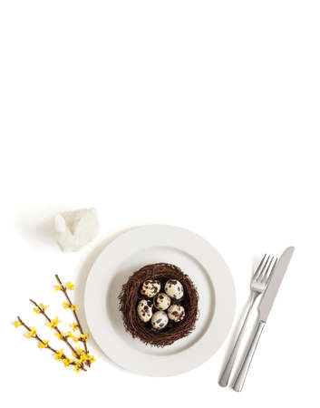 Spring Easter table setting with quail eggs in a nest on a plate, rabbit and yellow flowers on a...