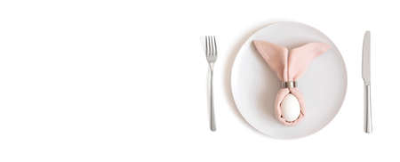 Beautiful Easter table setting with a white egg on a pink napkin with rabbit ears on a white...