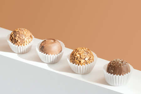 Chocolate truffles on a white stand on a brown background. Geometric composition with candies....