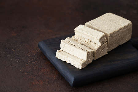 Sliced halva on a wooden tray on a brown background. Oriental sweets. Vegetarian dessert. Copy...
