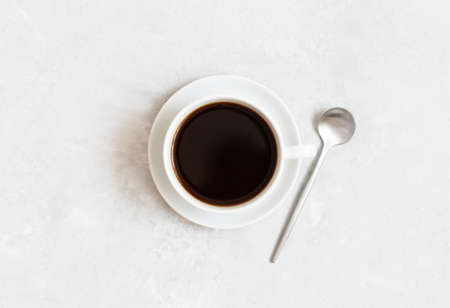 Black coffee in a cup and silver spoon on a white concrete background. View from above.の写真素材