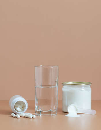 Collagen supplement. Collagen on a beige background. Collagen powder in a jar, pills and water closeup. Protein intake. Vertical orientation. Copy space.の写真素材