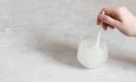 The hand mixes collagen powder or protein in a glass of water on a gray background. Healthy natural supplement concept. Space for text.の写真素材