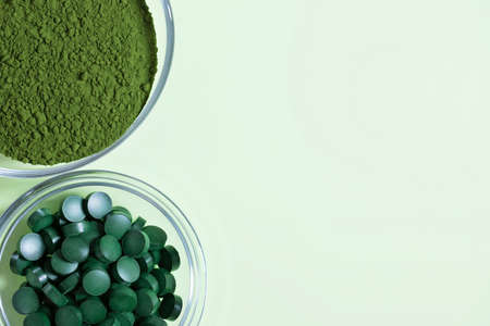 Chlorella powder and spirulina tablets on a green background. Organic food supplement. View from...