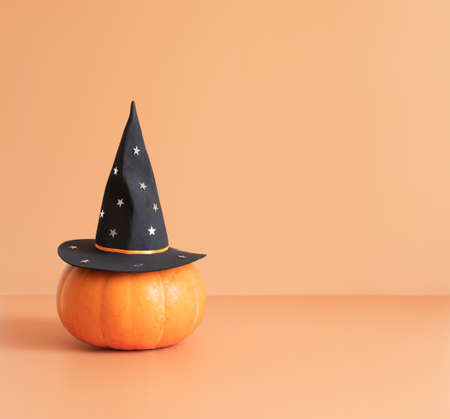 Halloween pumpkin in a black witch hat on a beige background. Halloween minimal concept. Copy space.