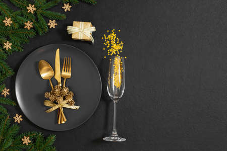 Christmas table setting with golden festive decorations on a black background. New Year party. Copy...