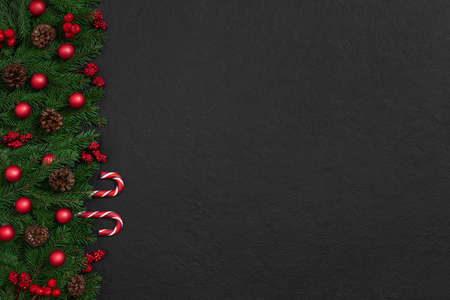 Christmas black background with fir branches, red baubles and lollipops. Happy New Year. Space for text. Top view, flat lay. Greeting card.の写真素材