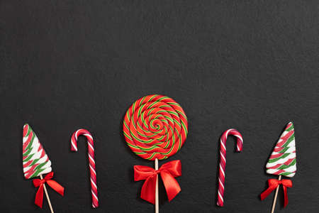 Christmas border with festive lollipops on black background. Christmas candy. Happy new year. Greeting card. Copy space, template. Top view, flat lay.の写真素材
